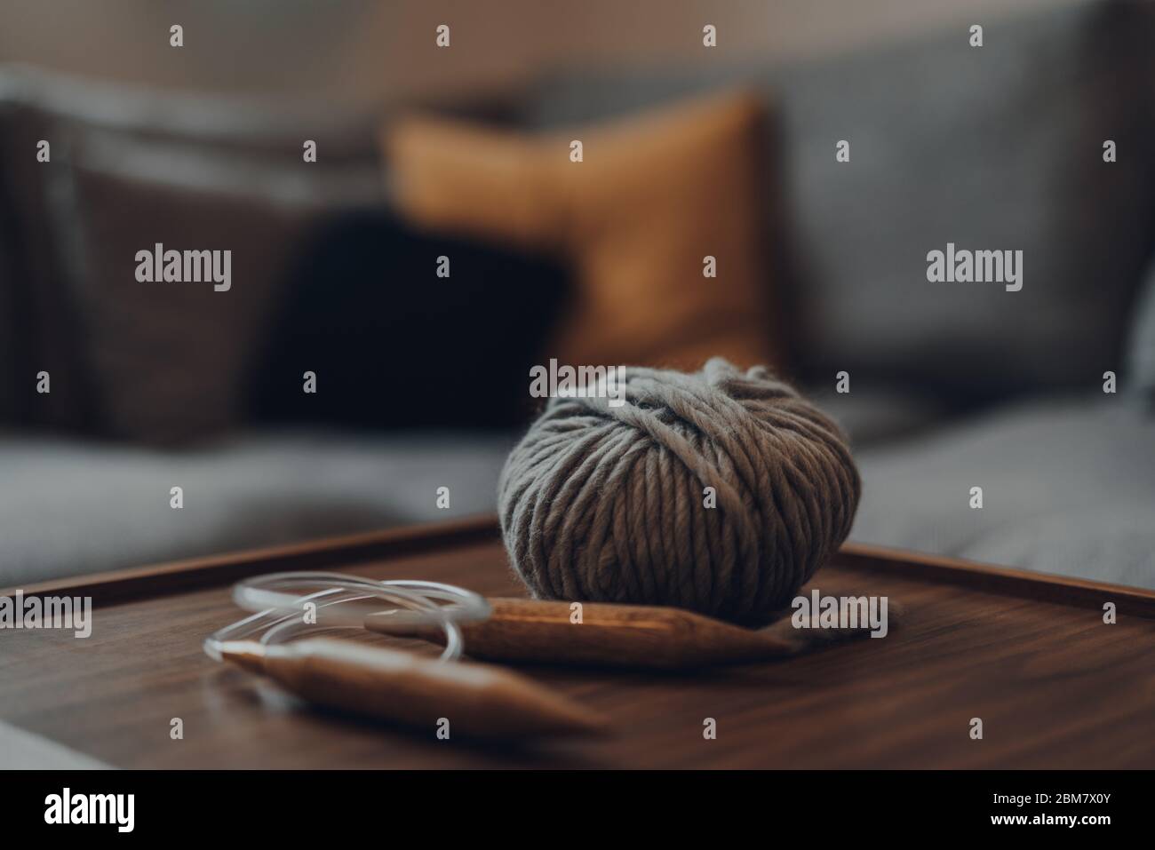 Close up of a ball of grey chunky wool yarn and large circular knitting needles on a wooden table, shallow focus, in modern Scandi interior. Stock Photo