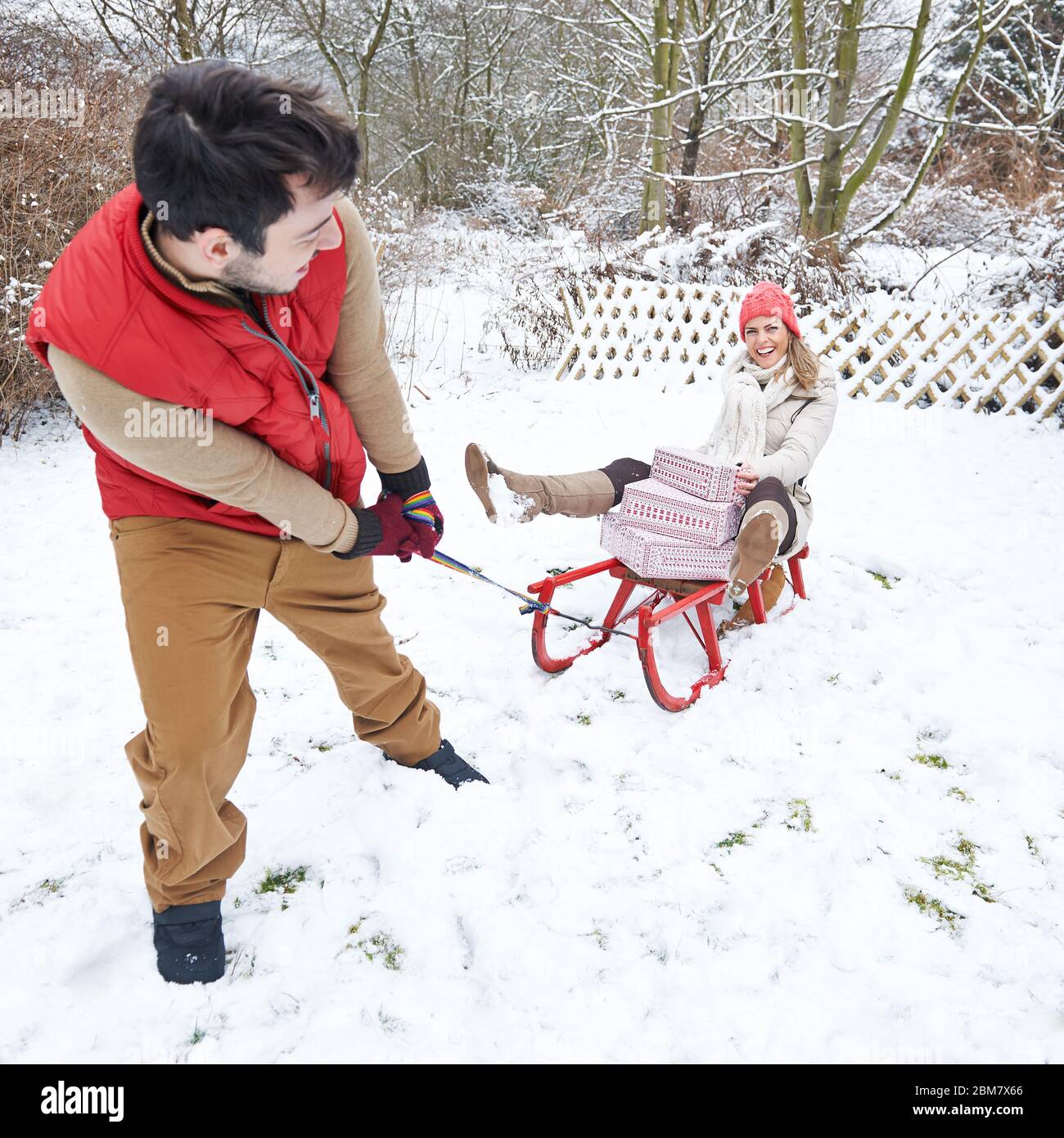 man-pulls-woman-with-gifts-on-sledge-in-the-snow-at-christmas-2BM7X66.jpg