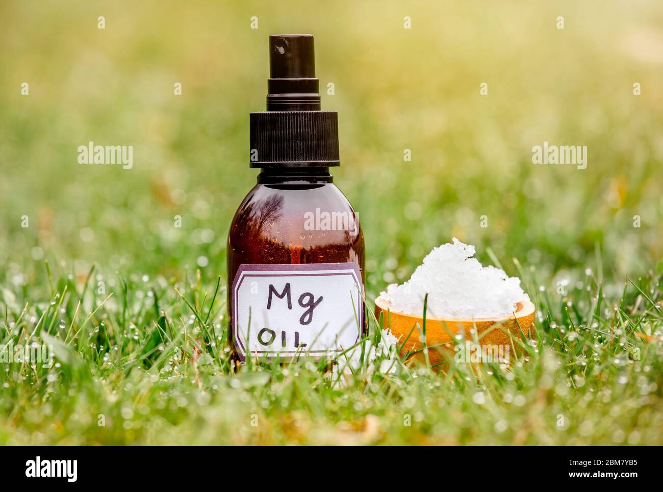 Magnesium Chloride Flakes on brown wooden cup with Magnesium vitamin oil in spray bottle in grass outdoors with blurred bokeh green background. Stock Photo