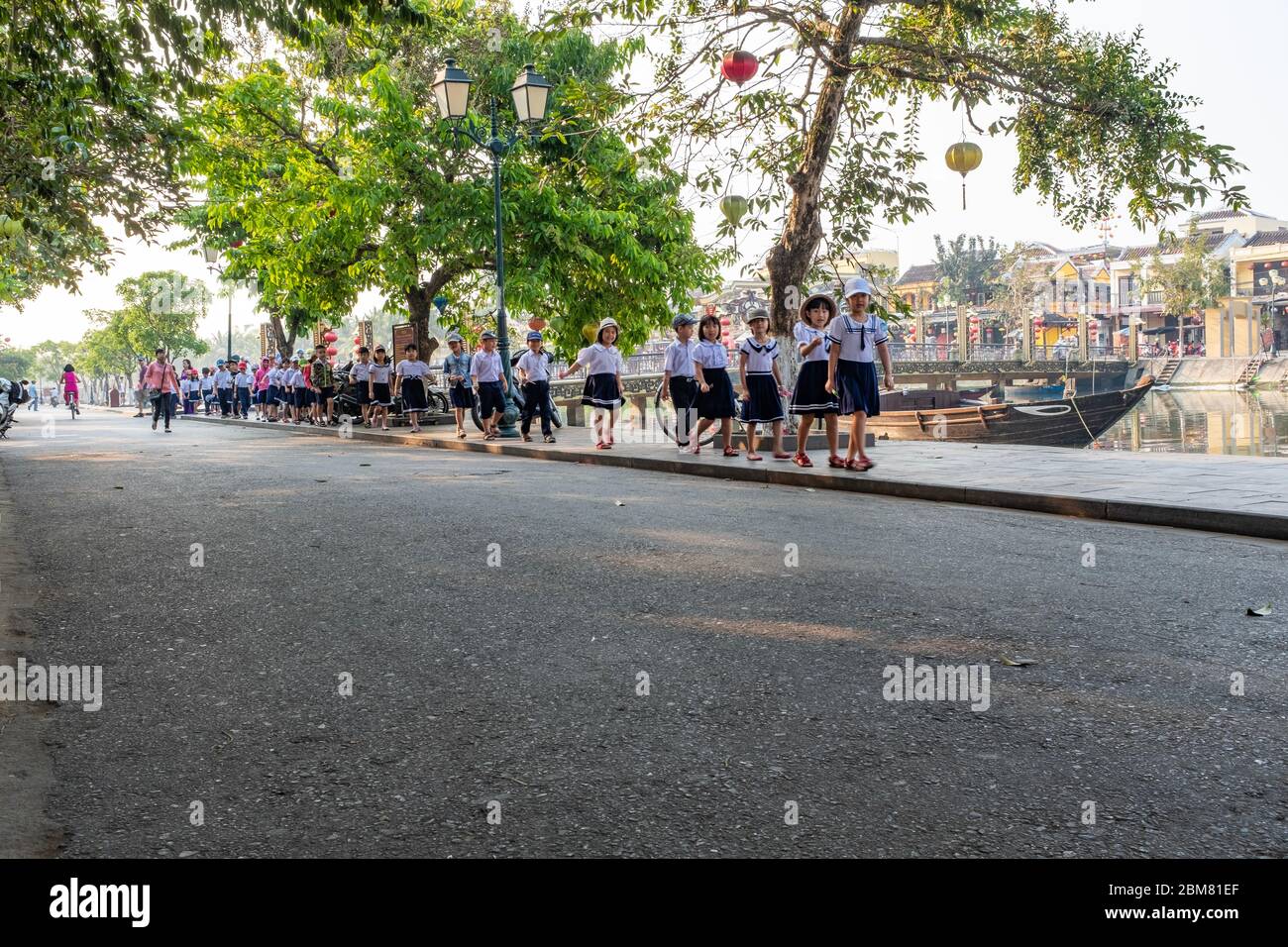 Hoi An, Vietnam - April 12, 2018: A street of Hoi An  in the morning, with school children in uniforms walking in a row and looking at the camera Stock Photo