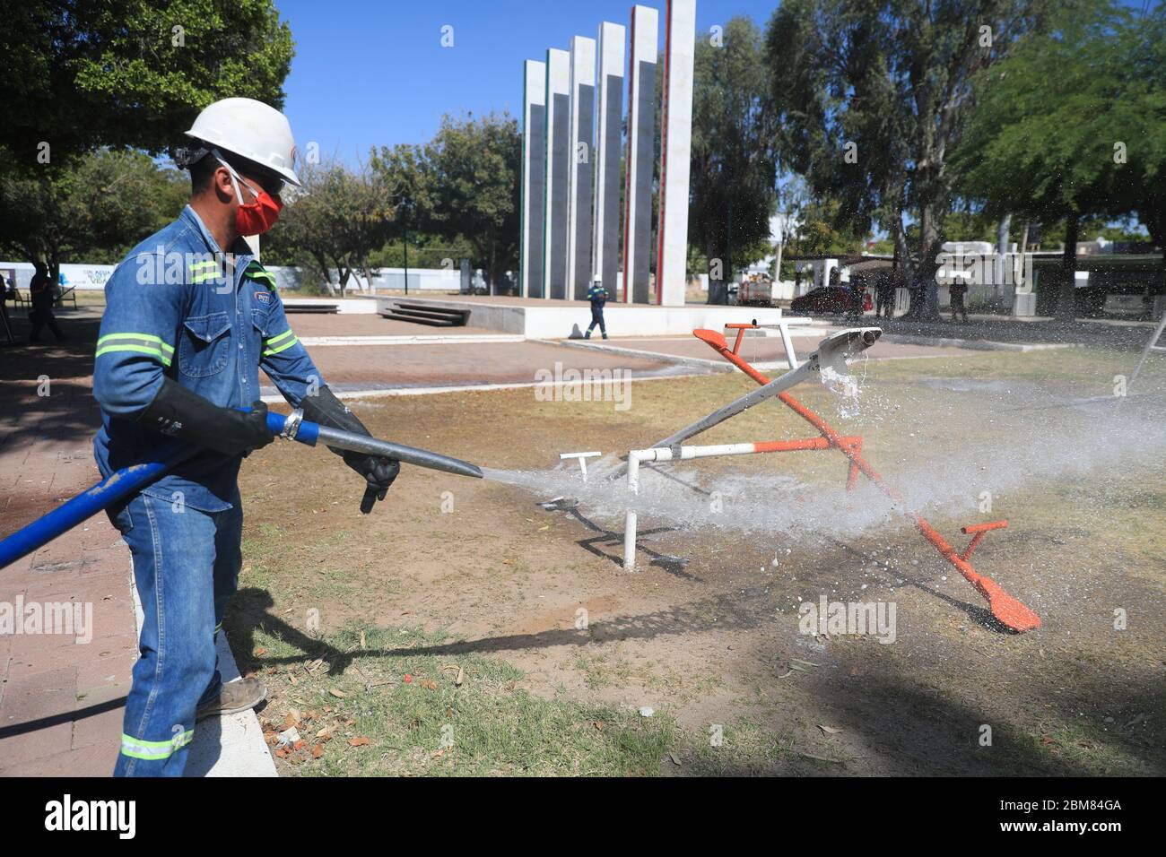 City council workers carry out sanitation work due to the Covid 19  pandemic, using pressurized liquids to clean the Niños Héroes public plaza.  They play games for children, trees, a statue and