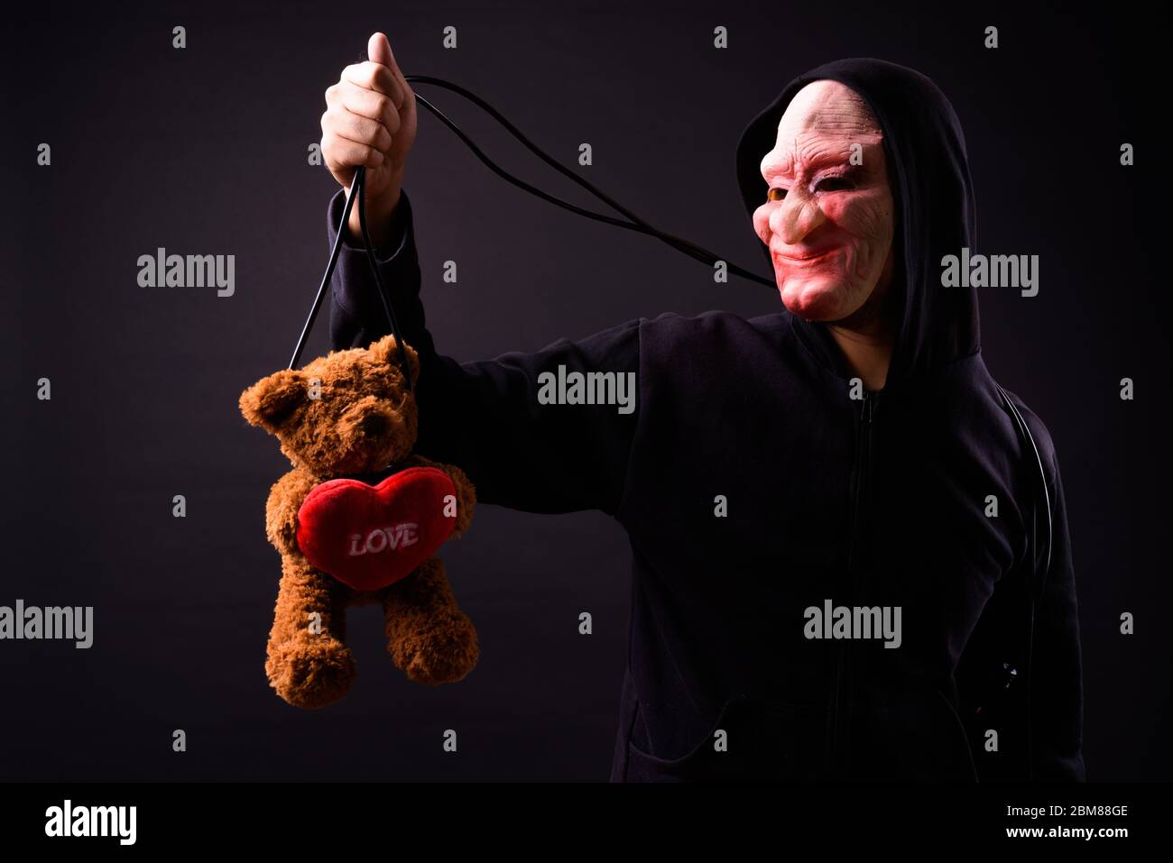Young man in hoodie and horror mask hanging teddy bear with string Stock Photo Alamy