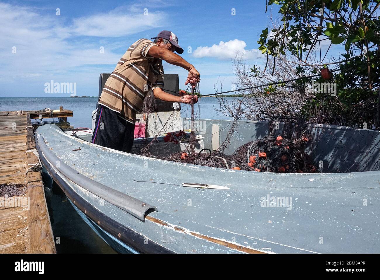 Artisanal fisher Dennis Arroyo Ramírez has fished with a nasa and a net since he was a child. On his boat on a wharf in Cabo Rojo, on Puerto Rico’s southwest coast, he fixes the net after a shark broke part of it. (Coraly Cruz Mejías, GPJ Puerto Rico) Stock Photo