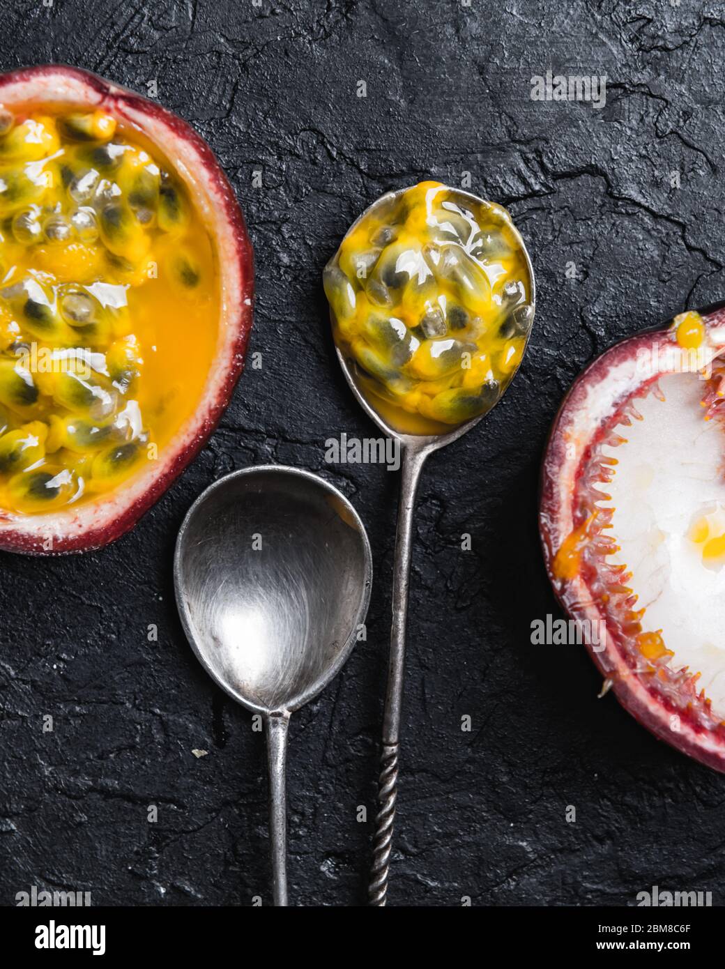 Slised passion fruit with silver spoons on black concrete background. Food photography Stock Photo