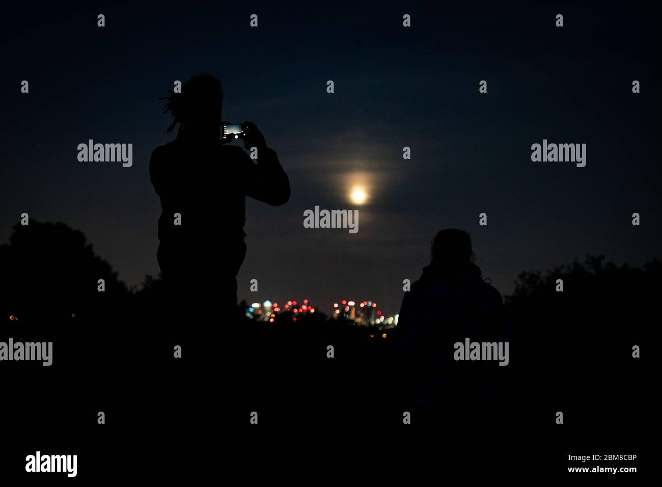 Members of the public attempt to photograph the final supermoon of the year. The full moon in May is also known as the 'flower moon', signifying the flowers that bloom during the month. Stock Photo