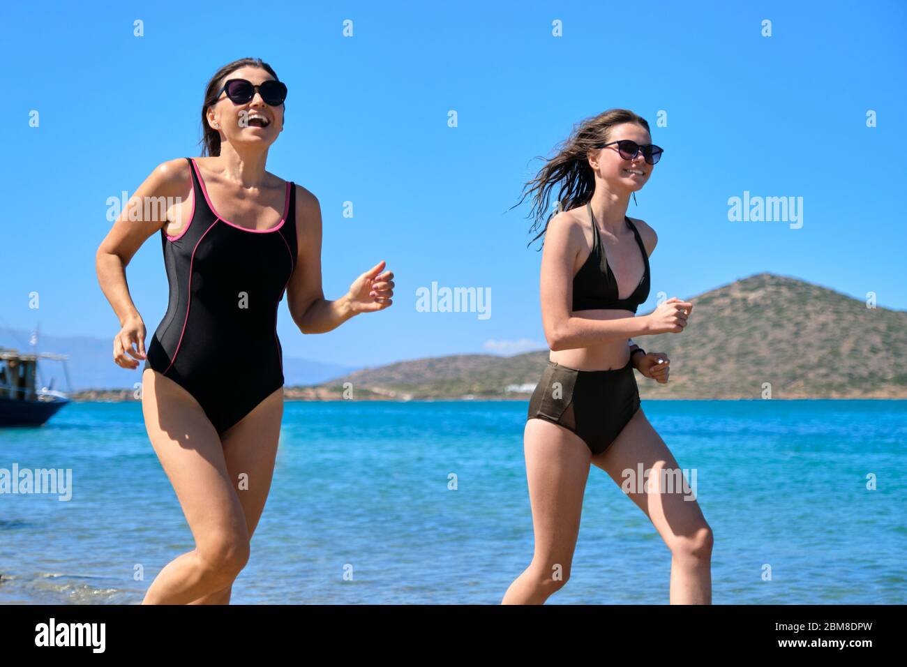 Mother And Teen Daughter Together On Beach Running By Sea In Swimsuit Stock Photo Alamy