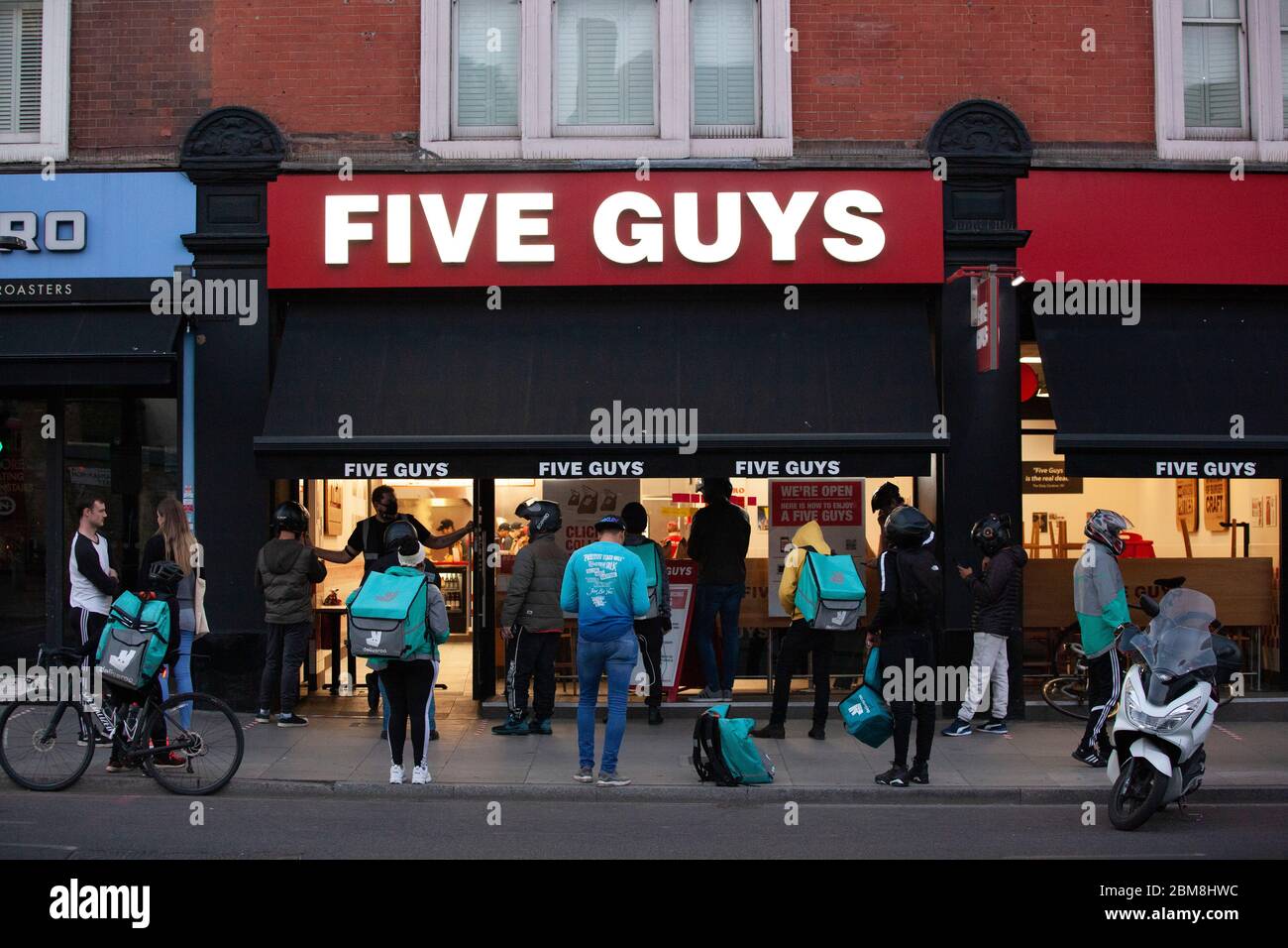 London, UK, 7 May 2020: on Clapham High Street, at a branch of Five Guys burger chain, many delivery riders and customers collecting online orders gather outside and social distancing rules are not strictly met. Anna Watson/Alamy Live News Stock Photo