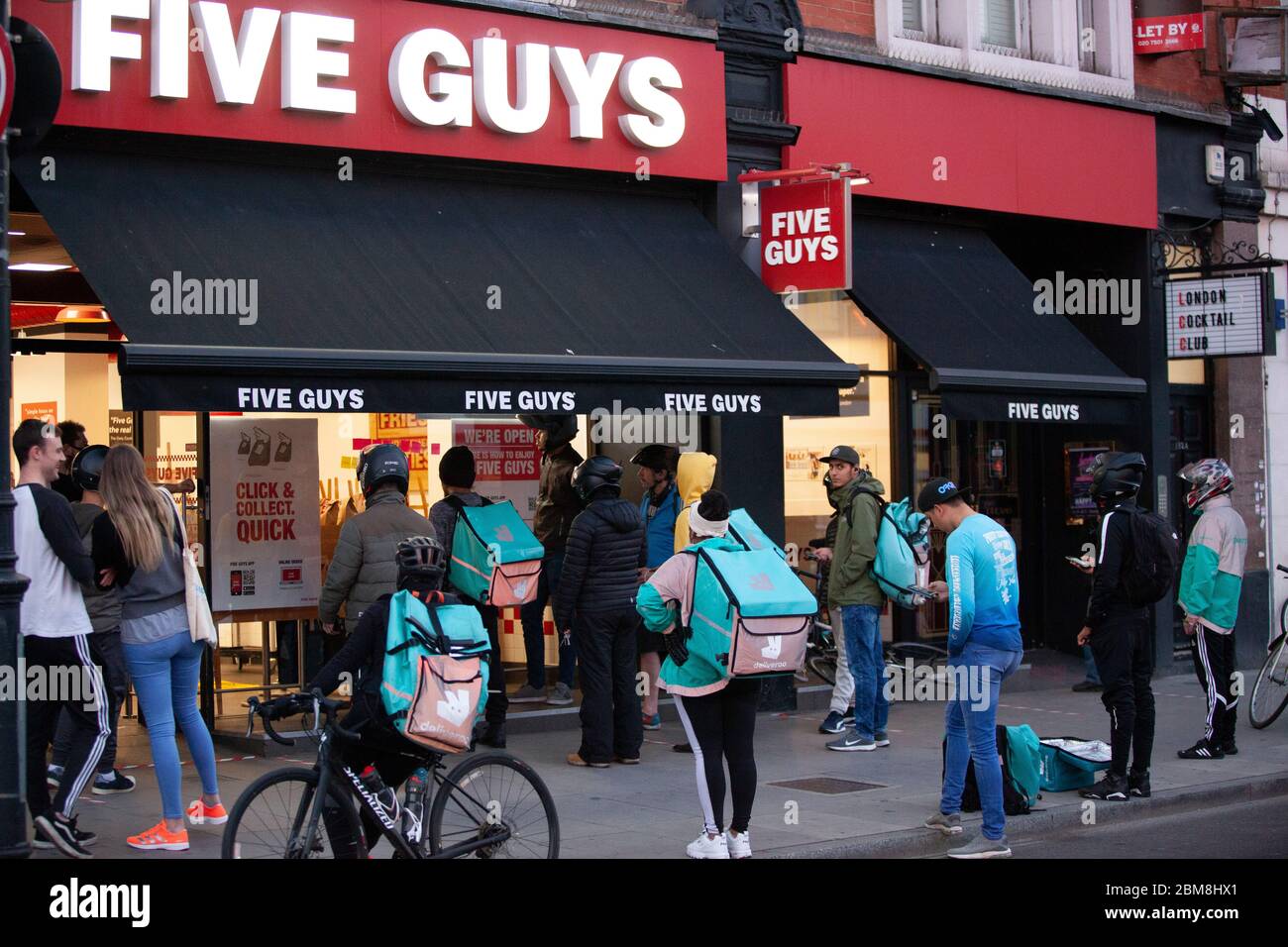 London, UK, 7 May 2020: on Clapham High Street, at a branch of Five Guys burger chain, many delivery riders and customers collecting online orders gather outside and social distancing rules are not strictly met. Anna Watson/Alamy Live News Stock Photo