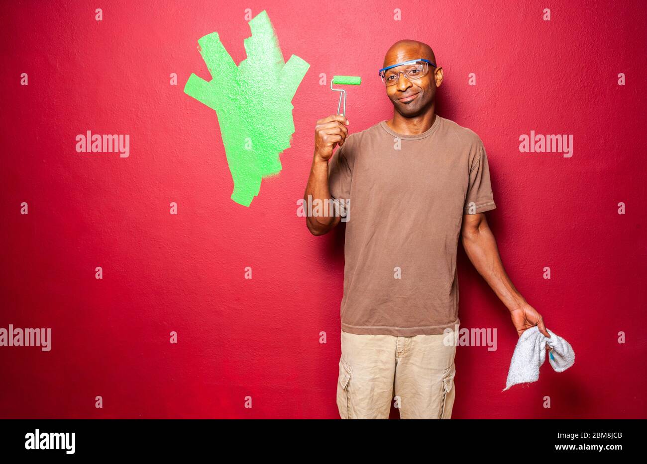 A man standing looking at the tiny paint roller in his hand as if it's insufficient for the job. Stock Photo