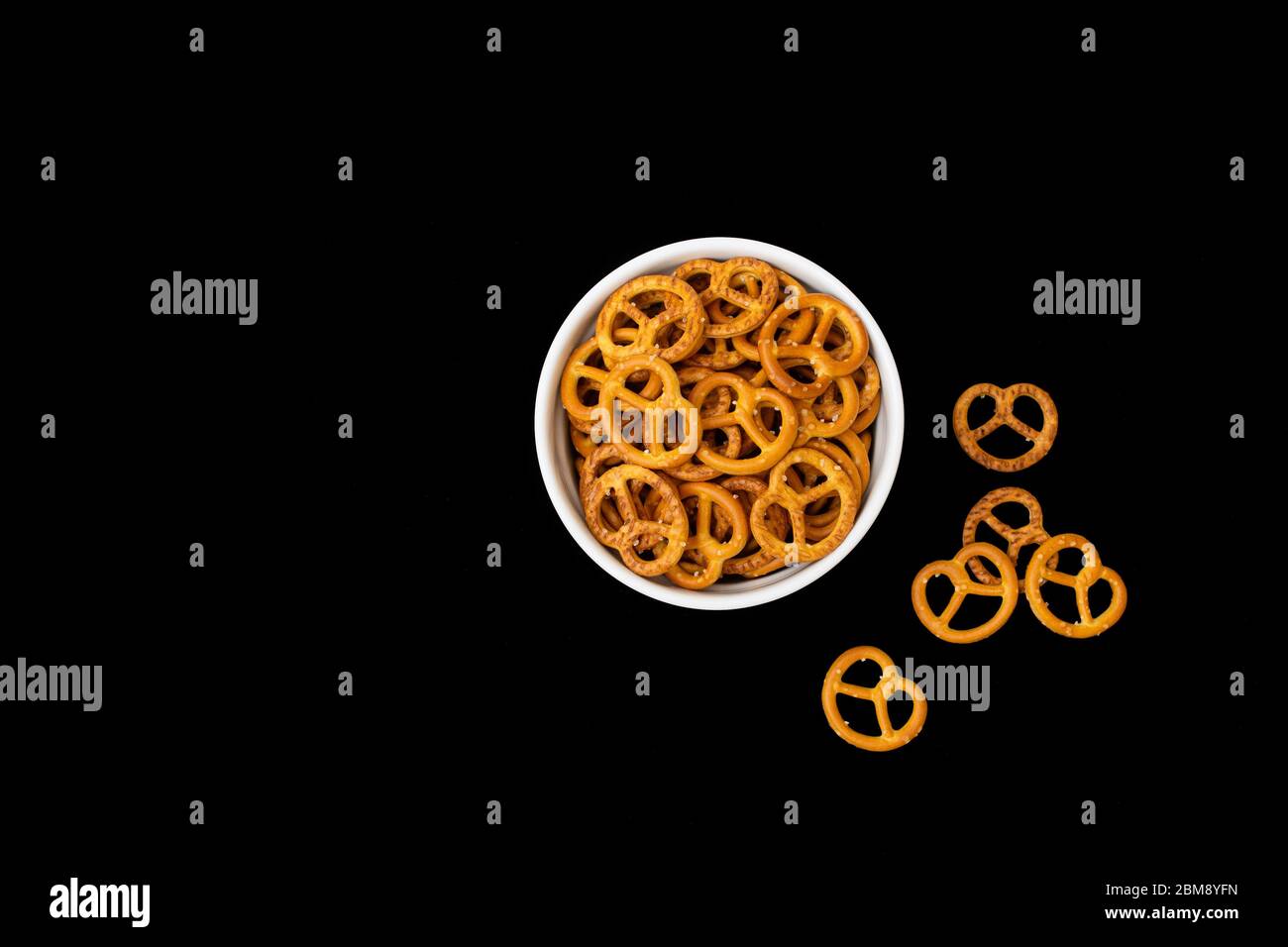 Salted pretzels in a white bowl isolated against a black background