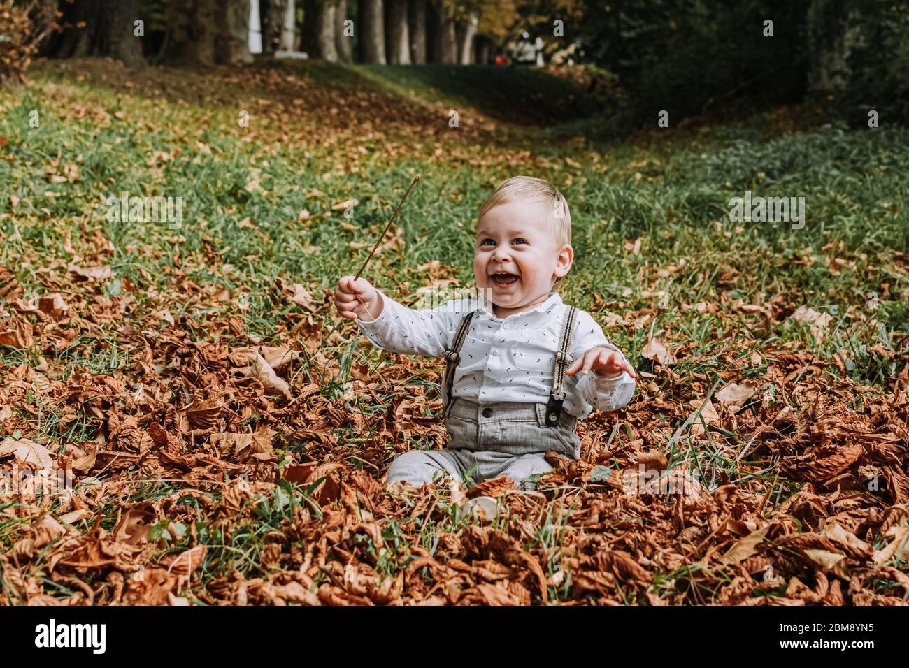 1 year old cute boy in stylish yellow jacket smiling and sitting on the grass in the park Stock Photo