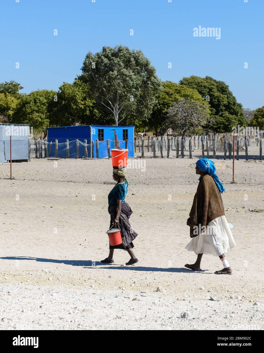 Two African woman walking with water buckets on their heads, walking to a village in Namibia, Africa. Stock Photo