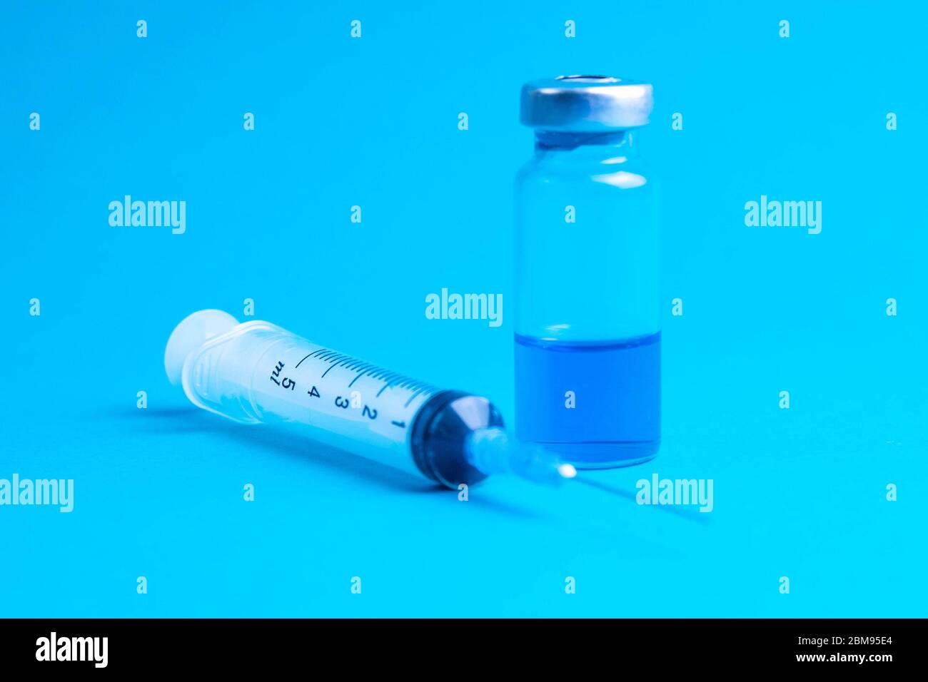 Glass vials and a medical syringe with a coronavirus vaccine on a blue ...