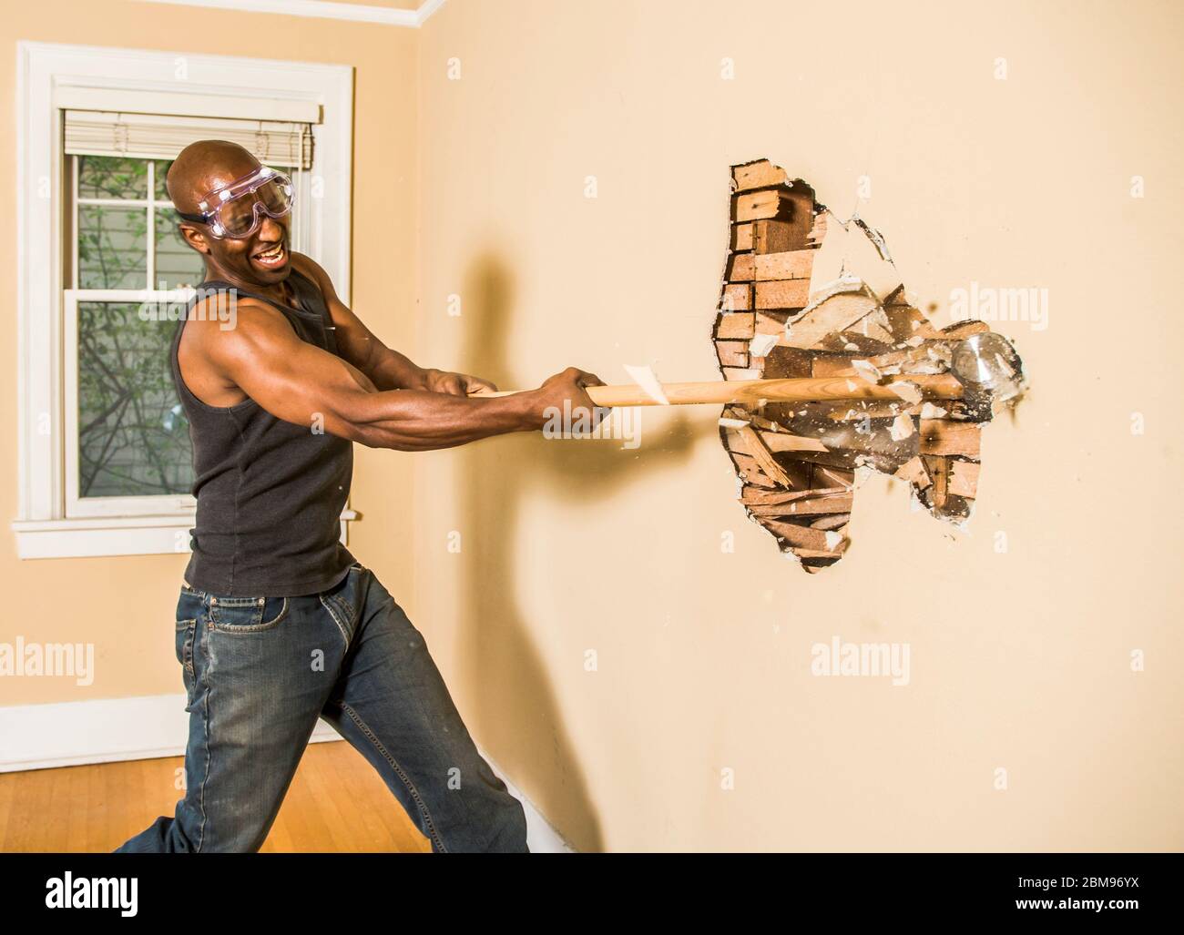 A man swings a sledgehammer at a interior wall of a home Stock Photo - Alamy