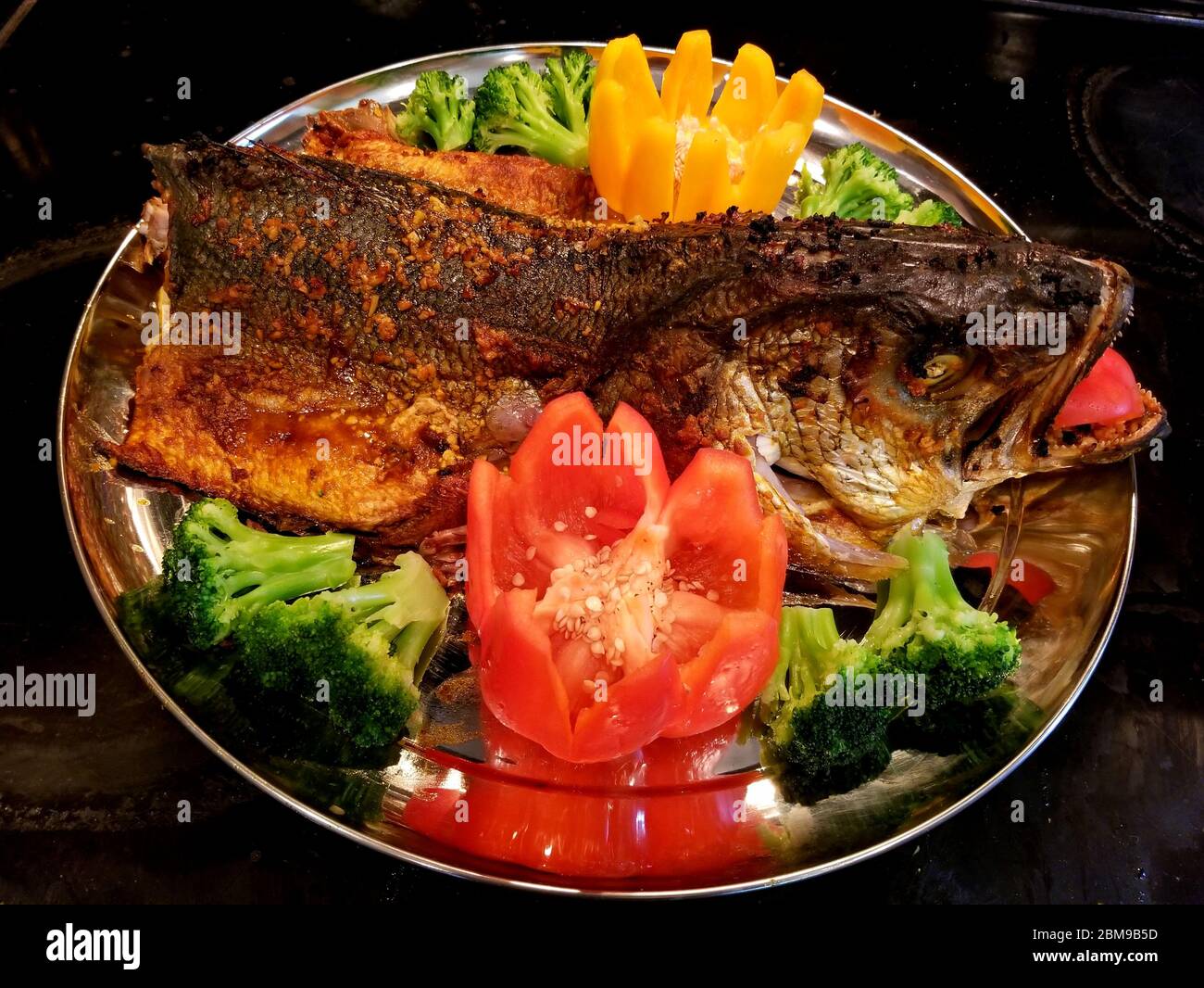 Oven-cooked bluefish head surrounded by broccoli and red peppers Stock ...