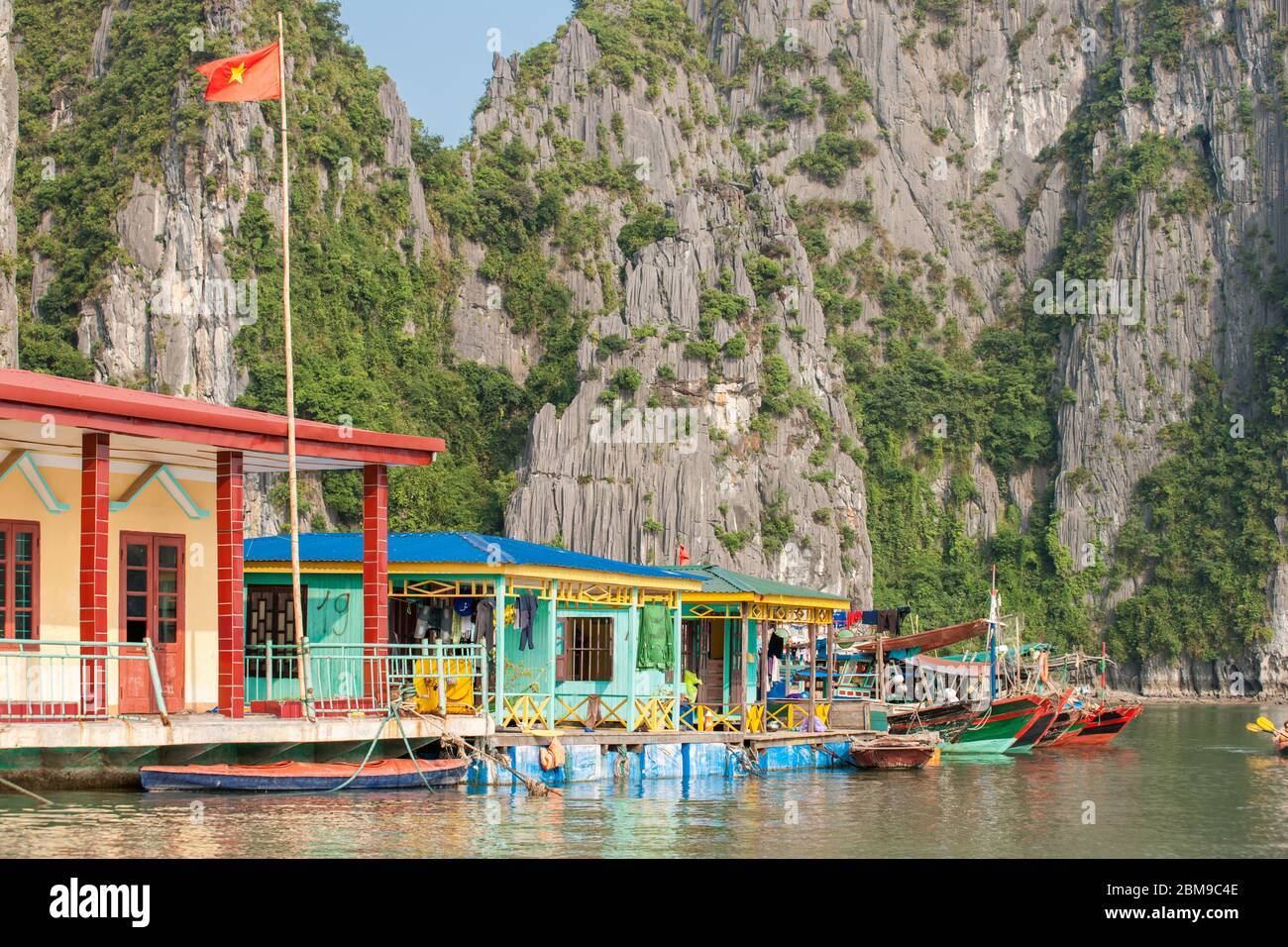 Halong Bay Vietnam - October 21 2013; Colorful homes of fishing people built over water against rock walls with fishing boats tied alonside. Stock Photo
