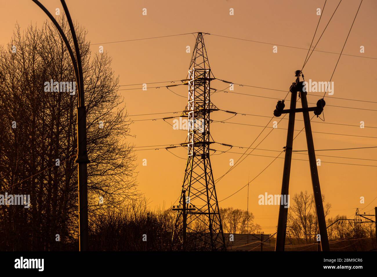 high-voltage poles of two intersecting power lines of different voltage against a sunset red sky Stock Photo