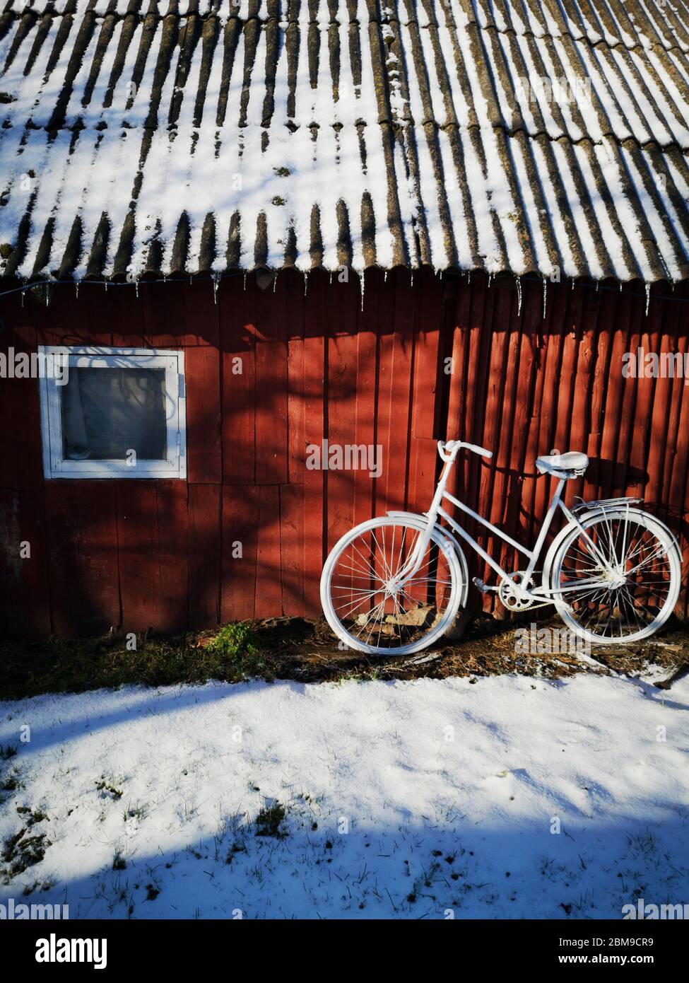 Decorative old painted in white bicycle near farm barn wall on snow Stock Photo