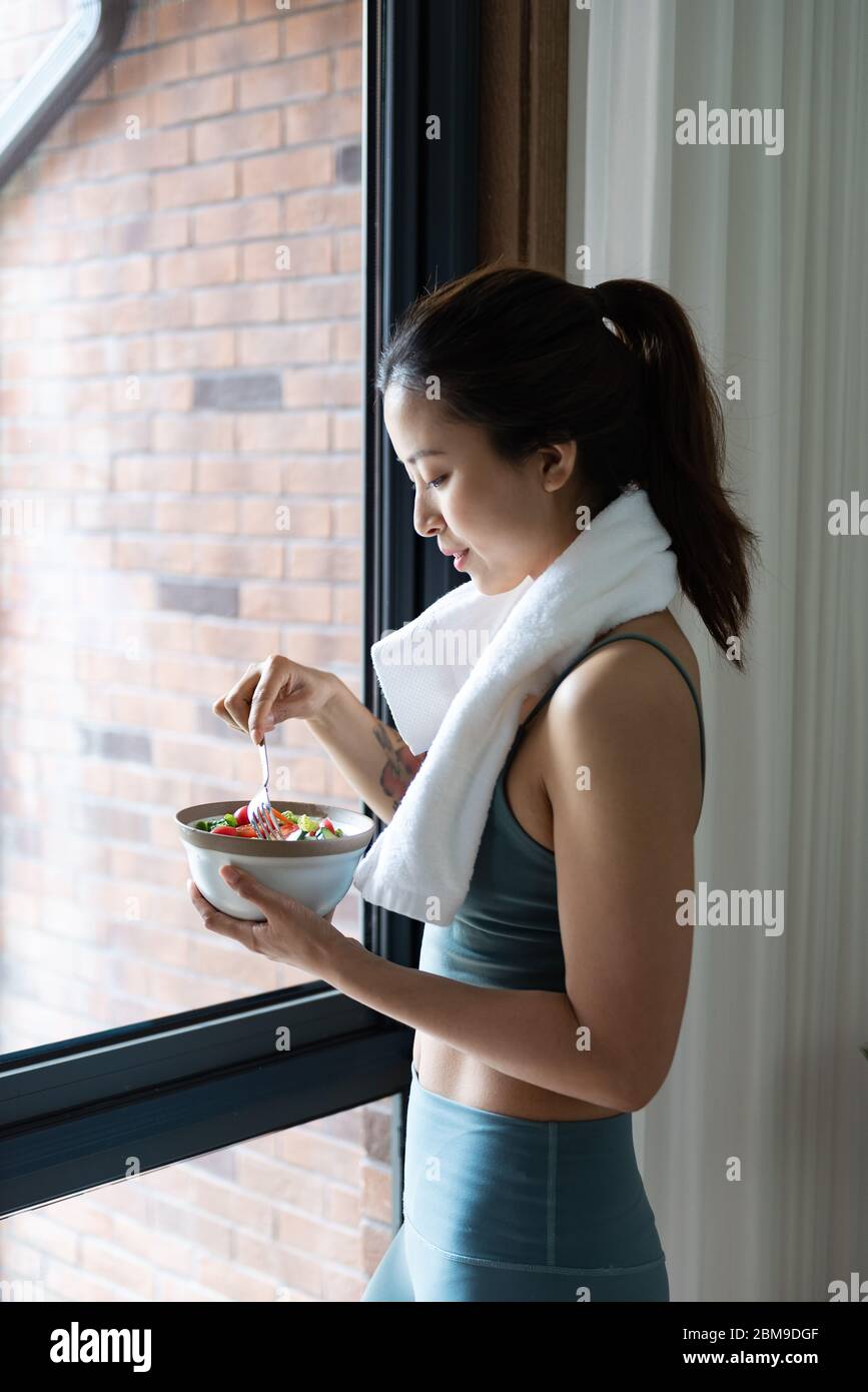 A young Asian woman eating healthy green vegetables by the window Stock Photo