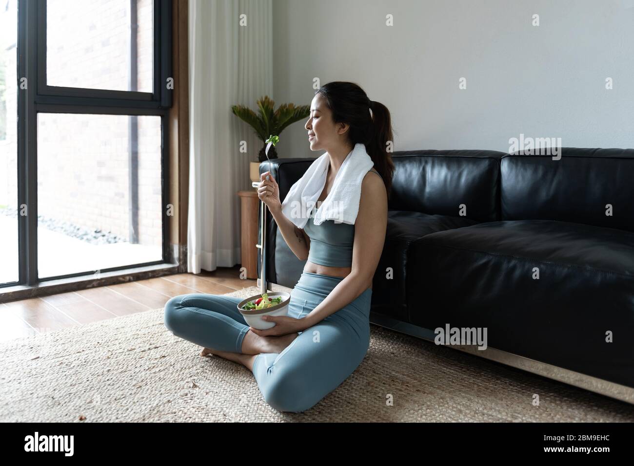 A young Asian woman eating a healthy vegetable salad in the living room Stock Photo