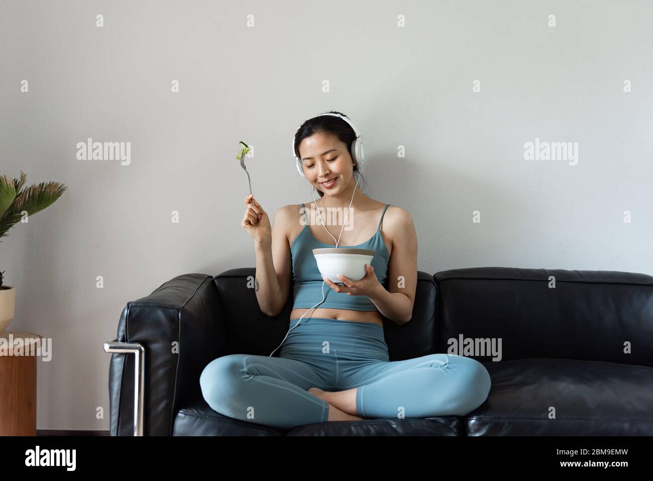 A young Asian woman eating a healthy vegetable salad in the living room Stock Photo