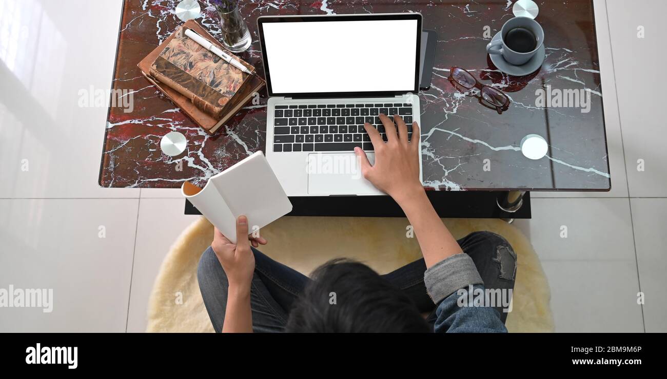 Top view image of smart man working as while sitting at the marble texture desk and typing on his mockup computer laptop over comfortable living room. Stock Photo