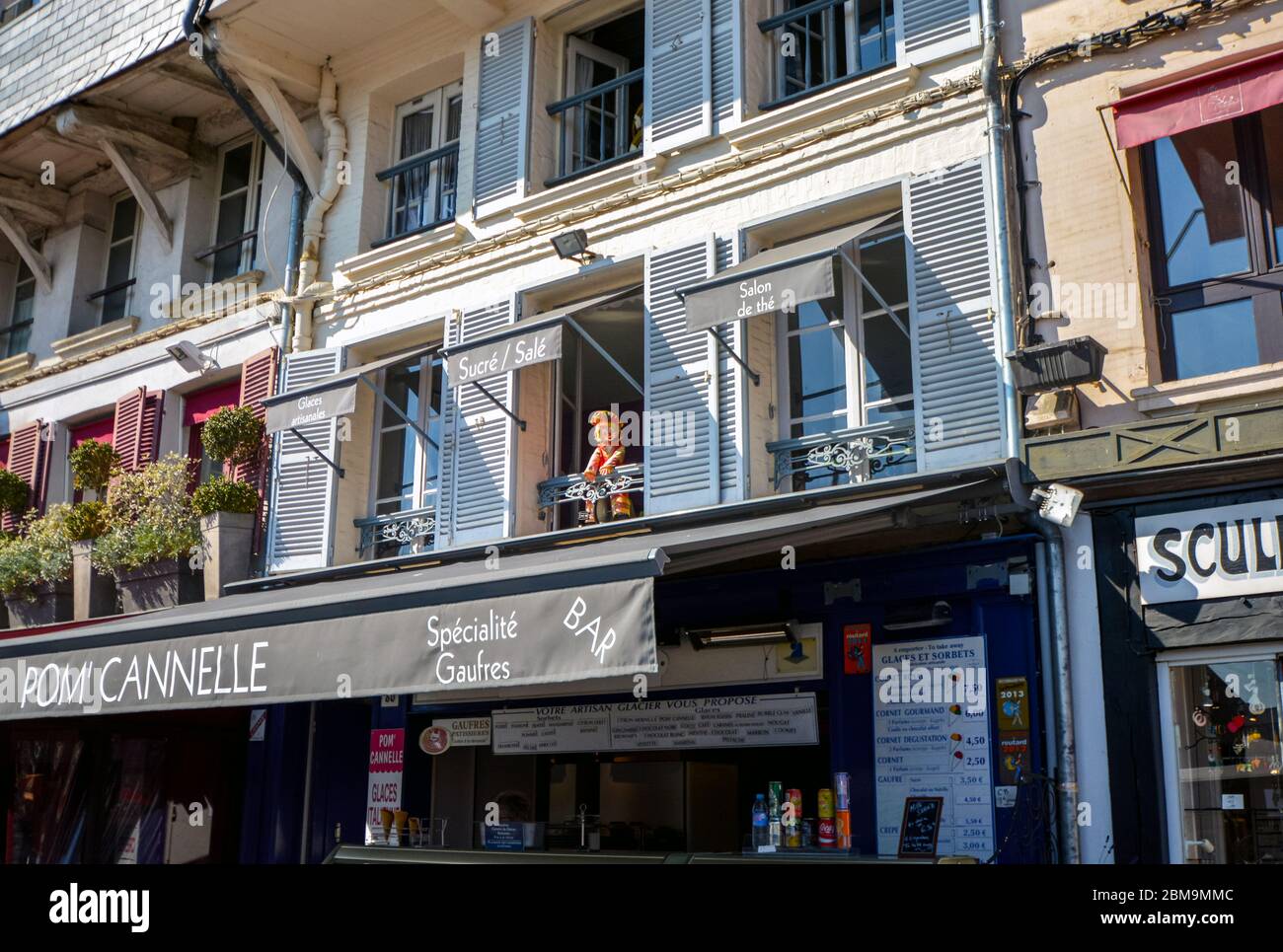 A clown doll looks down from a window above a sidewalk cafe in the seaside Normandy village of Honfleur France Stock Photo