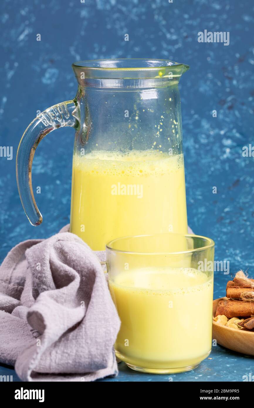 Organic turmeric milk. Decanter and glass with golden milk, napkin and ingredients on blue background. Concept of healthy eating, diet and detox. Sele Stock Photo