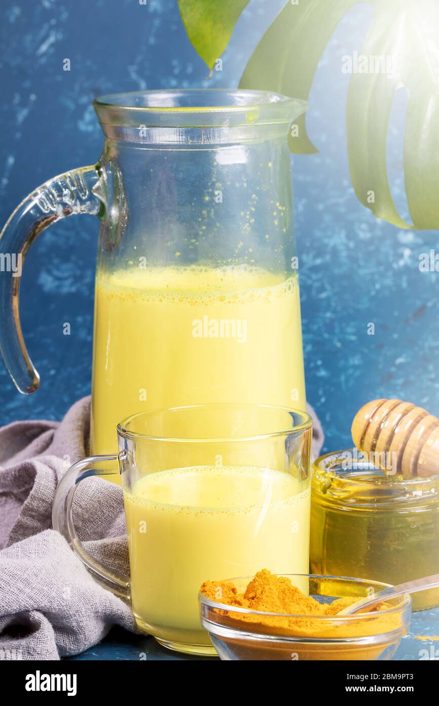 Turmeric milk. Decanter, glass with golden milk, curcuma powder and honey. Blue background. Concept of healthy eating, diet and detox. Selective focus Stock Photo