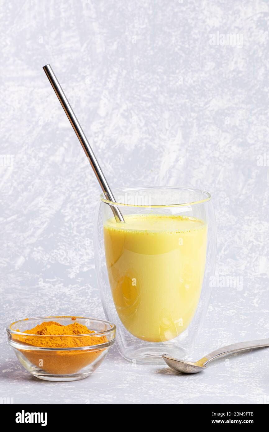 Organic turmeric milk. Glass with double walls with golden milk and metallic drinking straw on light grey. Healthy eating and detox. No plastic and ze Stock Photo