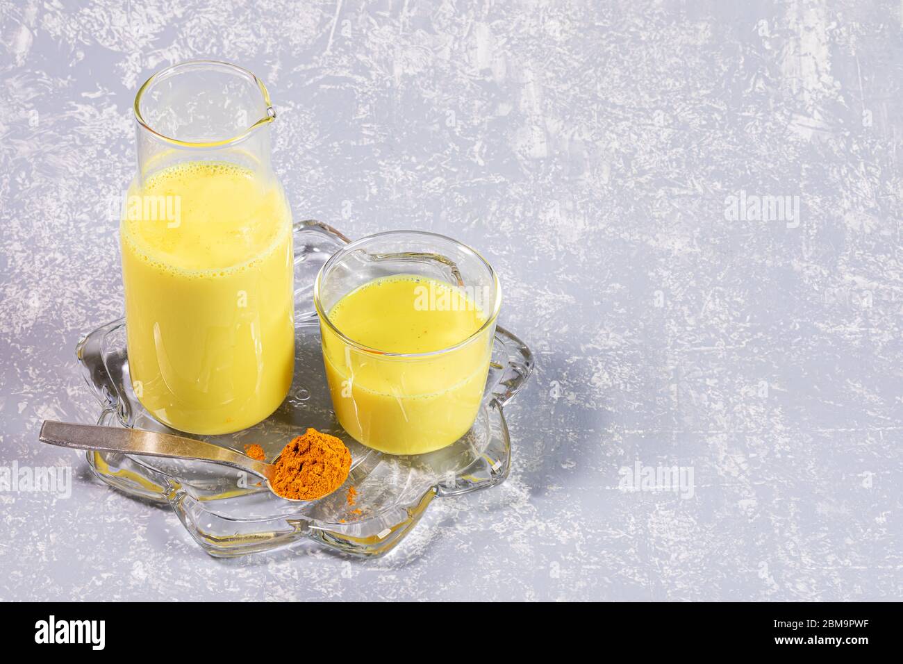 Organic turmeric milk. Bottle and glass with golden milk on figured transparent plate on light grey background. Concept of healthy eating, diet and de Stock Photo