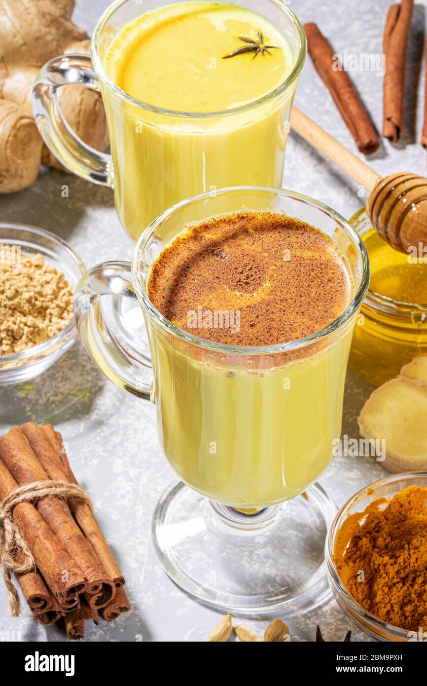 Ayurvedic turmeric milk. Two glasses for mulled wine with golden milk with ingredients on light grey. Alternative medicine. Healthy eating and detox. Stock Photo