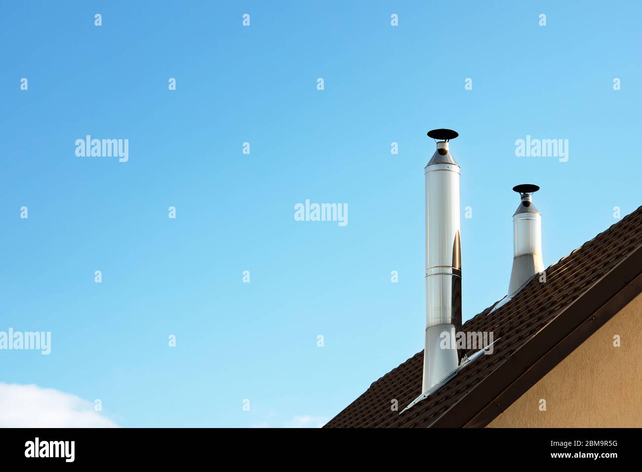 Two modern style chimneys from oven and fireplace stacked stainless steel on tiled roof made according to fire safety requirements, and to avoid conde Stock Photo