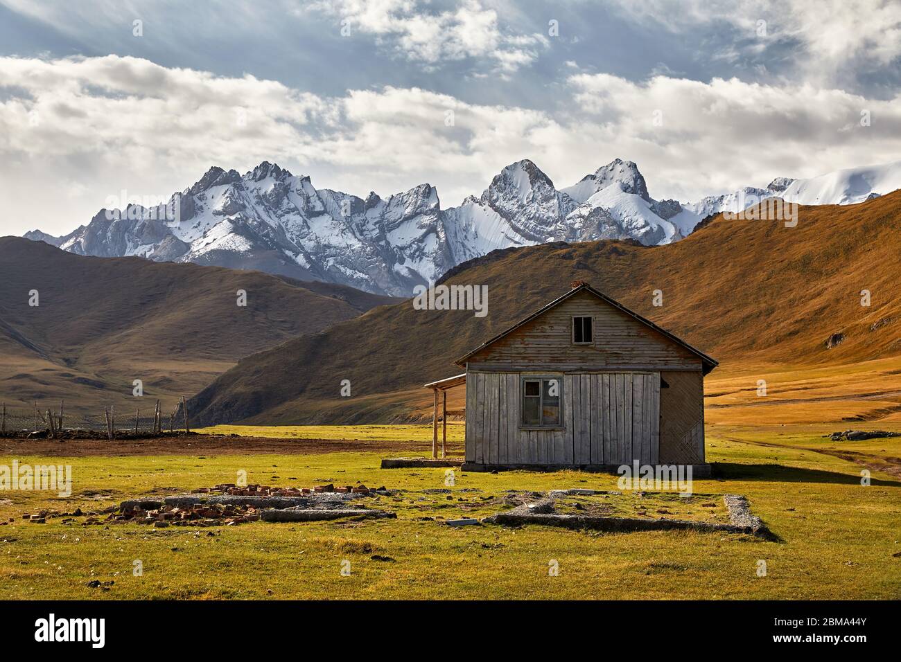Old rustic wooden house white in the valley with snow mountain peaks near Kel Suu Lake in Naryn region, Kyrgyzstan Stock Photo