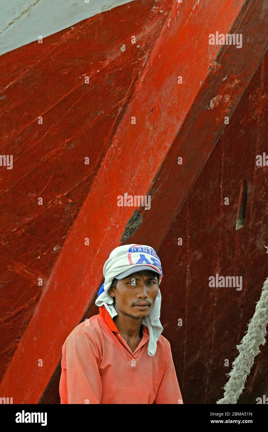 jakarta, indonesia - 2009.11.17: a port worker sitting in front of the bow of a wooden prahu pinisi (kapal layar motor klm) berthed at sunda kelapa po Stock Photo