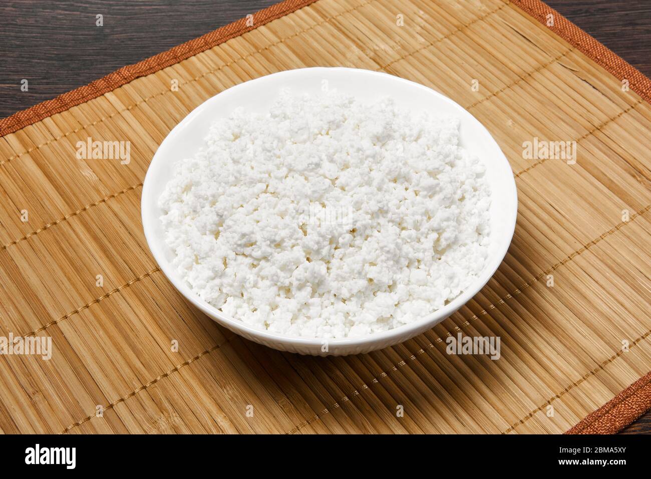 bowl with grainy cottage cheese on a straw tablecloth mat on the table Stock Photo