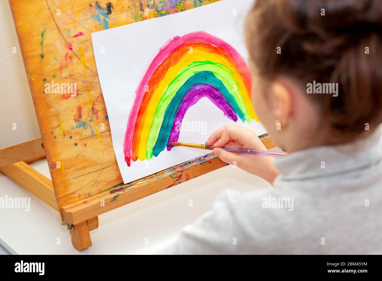 Child is drawing rainbow with watercolors on the sheet of paper on the easel. Creativity concept. Stock Photo