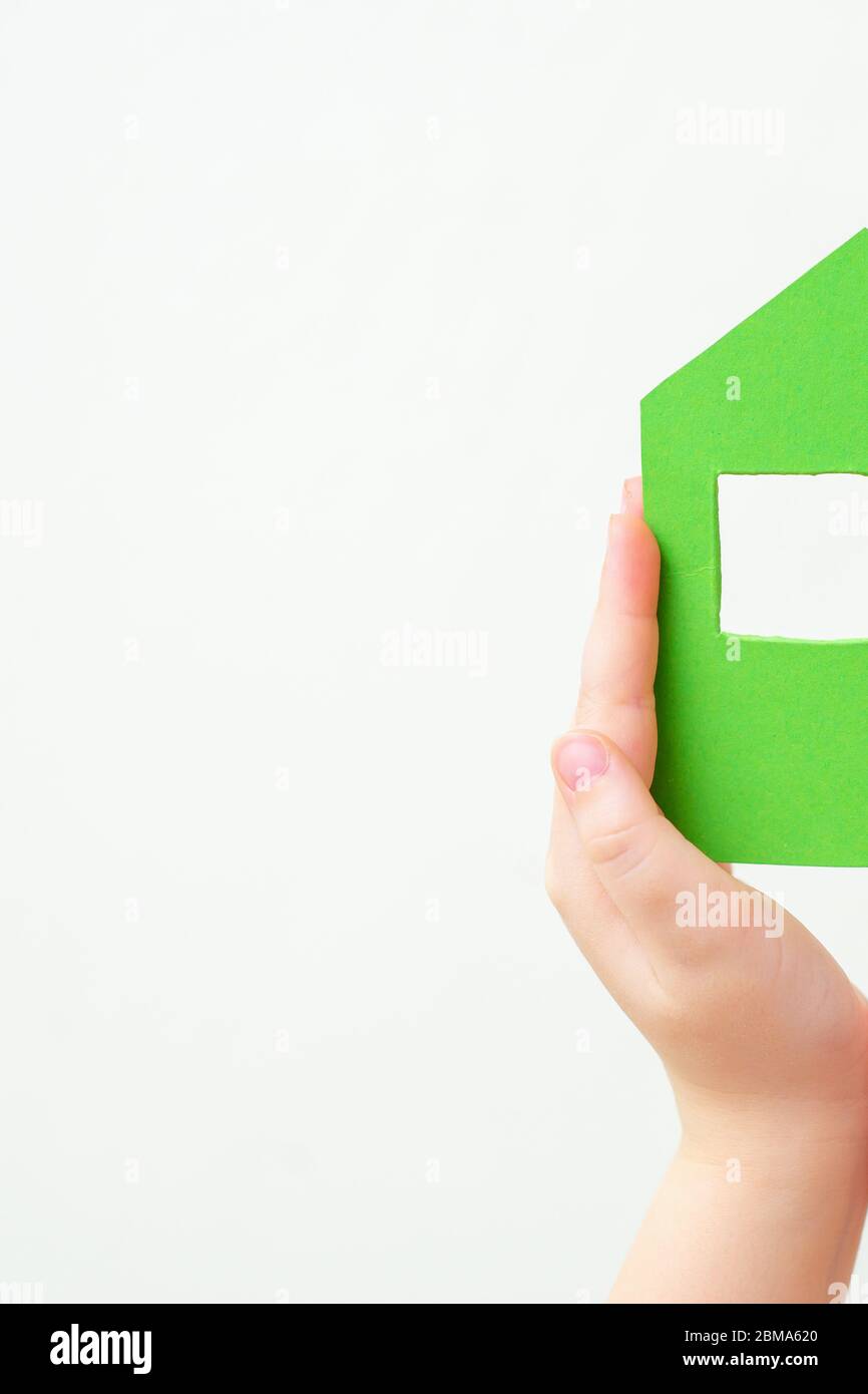 Children's hands holding a half of paper green house on white background with copy space. Stay home concept. Stock Photo