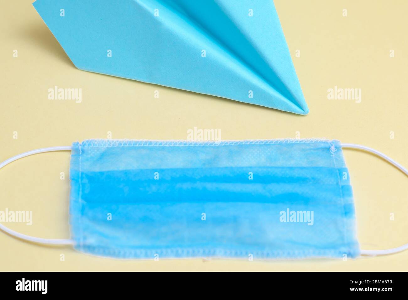 Paper blue airplane with medical blue mask on yellow background. Copy space. Stock Photo