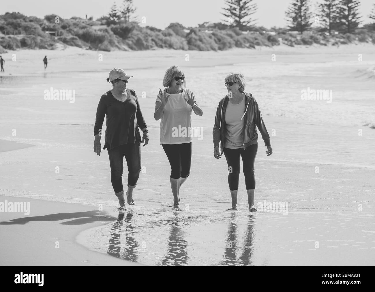 Lovely group of three active senior woman on their 60s walking, exercising and having fun on the beach. Mature females Laughing enjoying walk on vacat Stock Photo