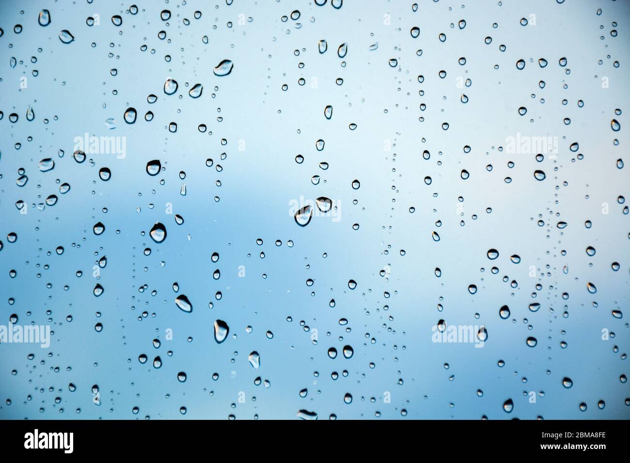 Drops of rain on a window glass. Beautiful blue cloudy sky in background. Stock Photo