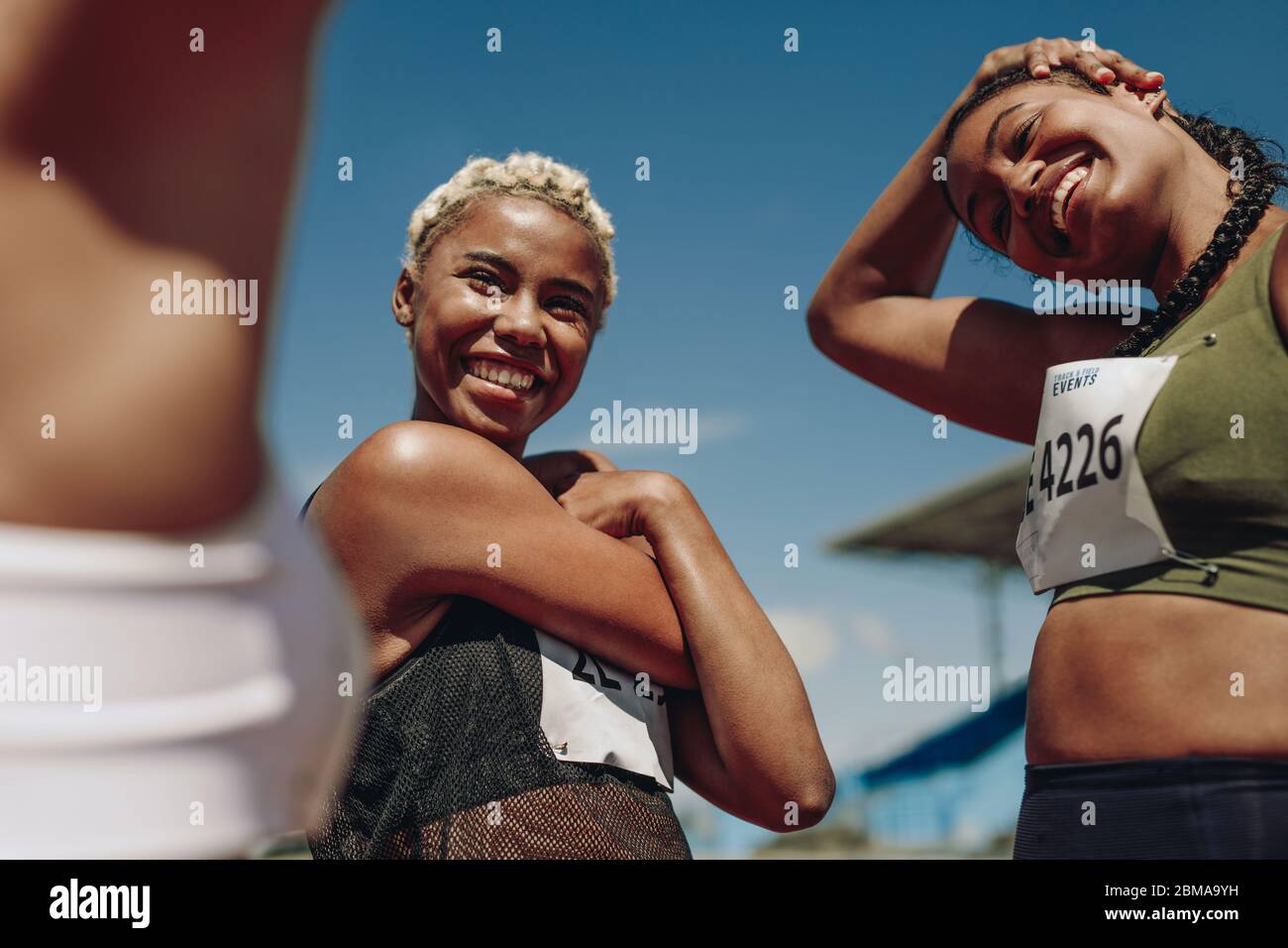 Group of female sprinters warming up before the competition. Female athletes stretching arms before the race. Stock Photo