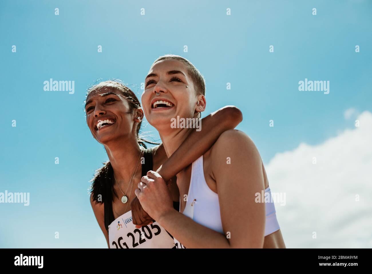 Two young woman athletes smiling outdoors. Female runners looking happy after winning the competition. Stock Photo