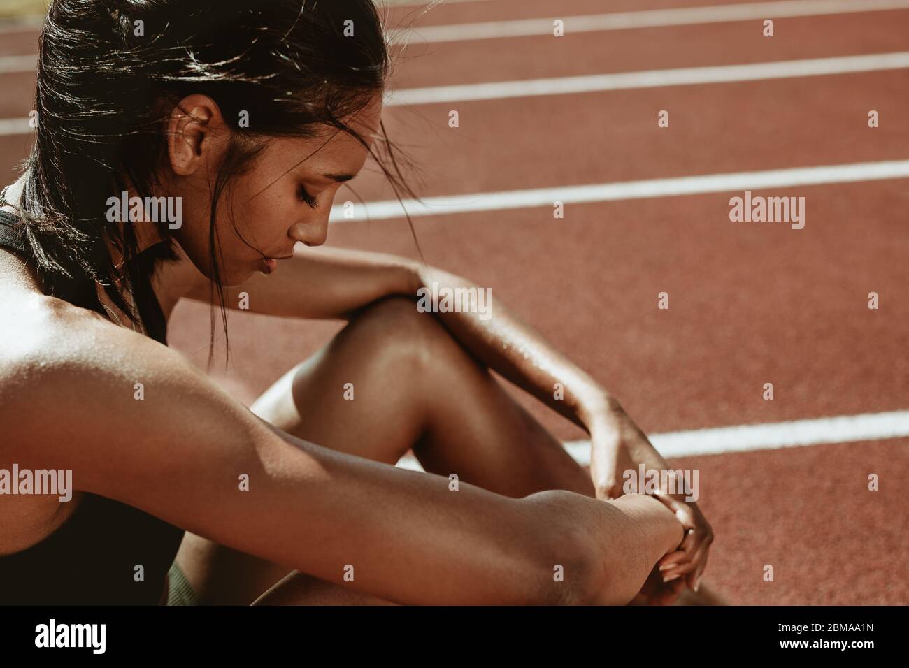 Female runner looking tired after workout session. Sportswoman feeling exhausted after a training session at running track. Stock Photo