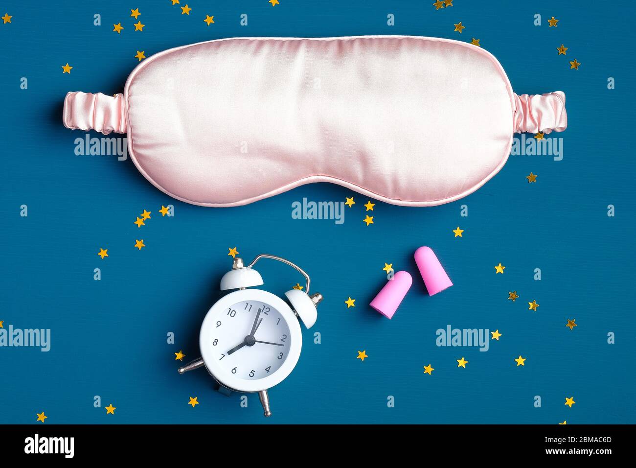 Sleep eye mask with alarm clock and ear plugs on dark blue background