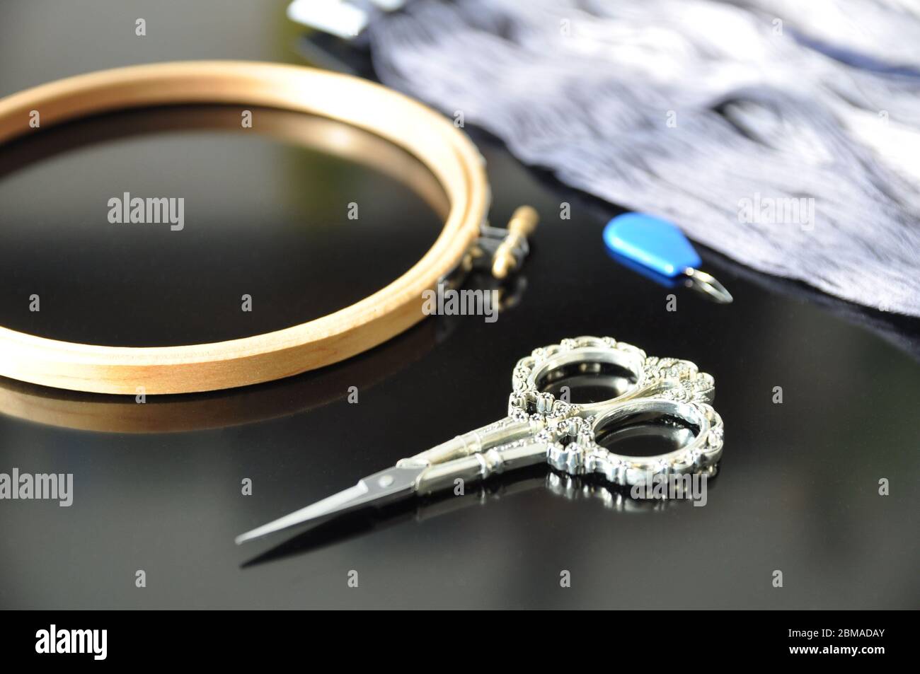 Accessories for needlework. Hoop, multi-colored threads, scissors, needle-threader on a black background. Copy space. Stock Photo