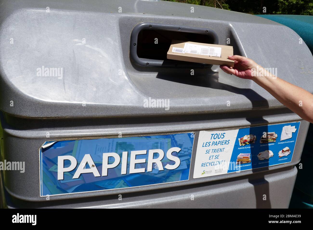 Glass bottle with female hand being placed into Large plastic recycling bin in the Ariege region of southern France Stock Photo