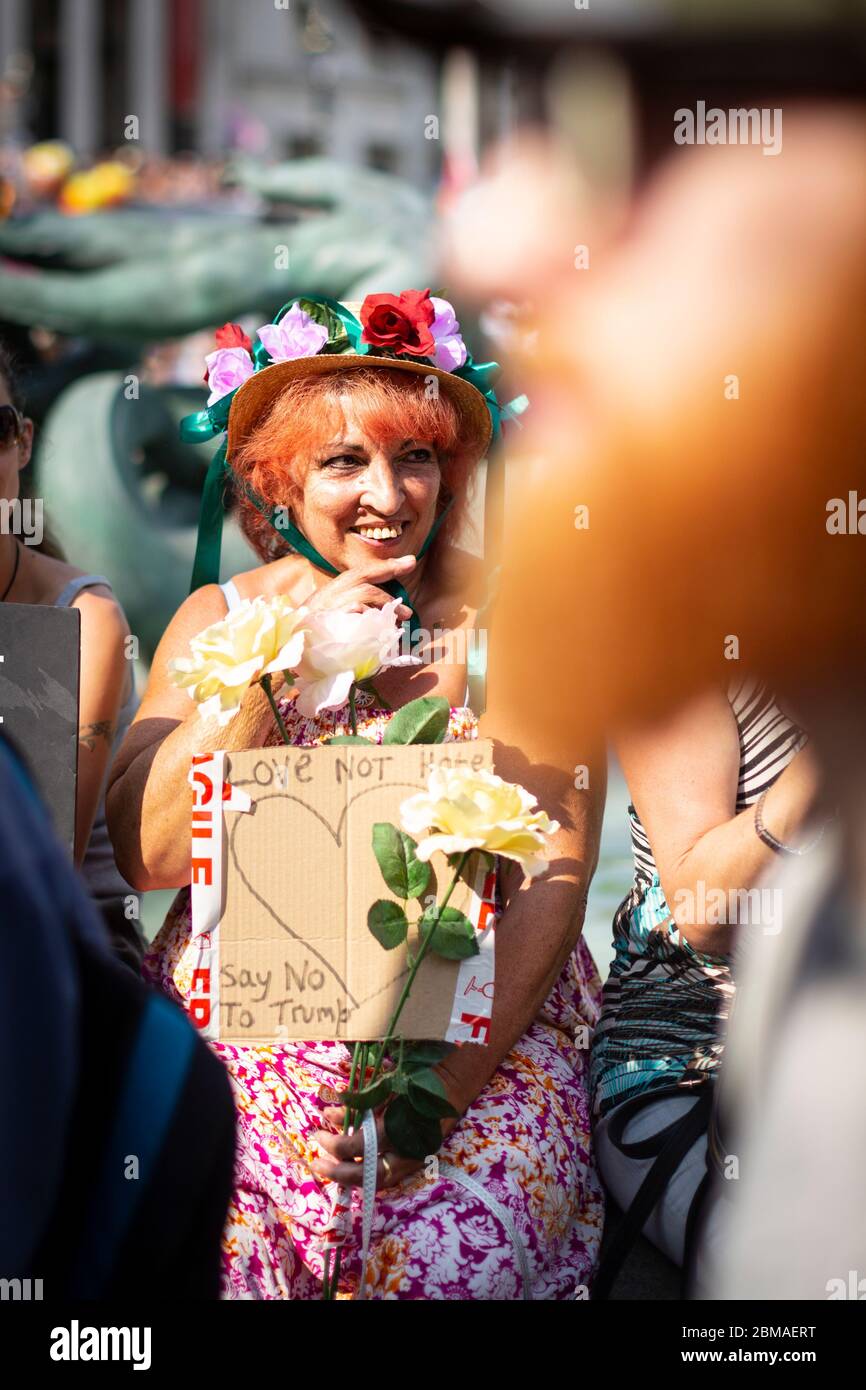 A woman with red hair and wearing a floral wreath holds a sign reading 'Love not Hate' at the protest against Donald Trump's visit to London, 2018 Stock Photo