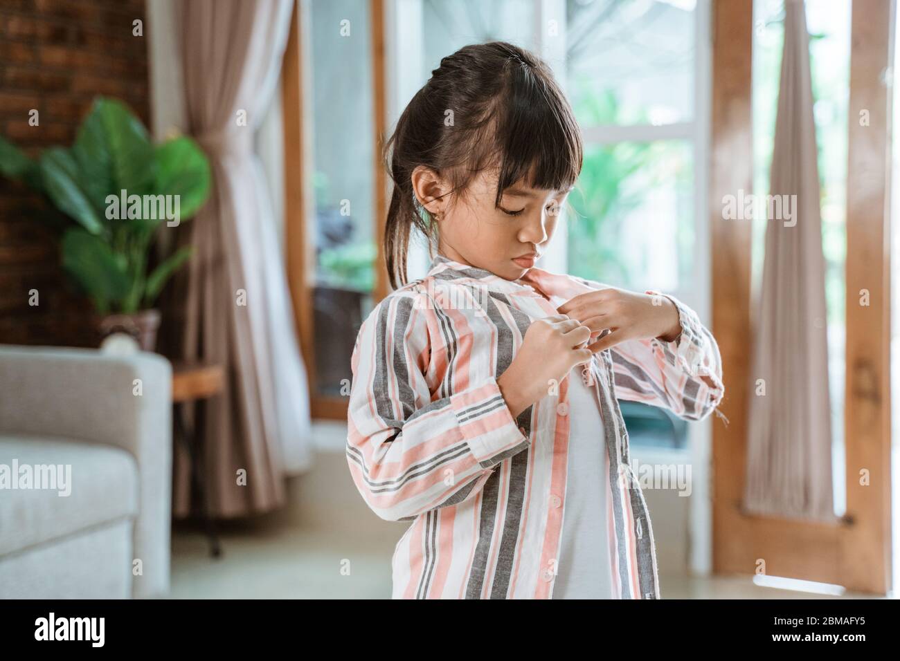 asian little girl putting her clothes on by herself in the morning