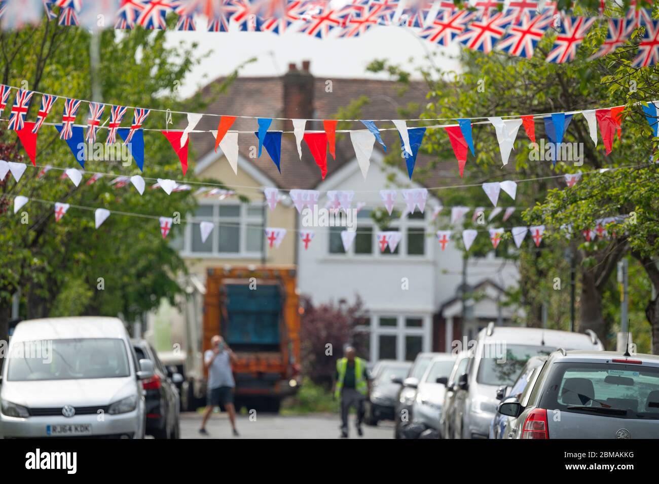Merton Park, London, UK. 8 May 2020. Bunting along the length of a leafy south London street on day 46 of the Coronavirus lockdown to commemorate the 75th anniversary of VE Day is organised by AFC Wimbledon Foundation Dons Local Action in conjunction with Old Rutlishians whose rugby club borders the street in Merton Park. Unfortunately the low slung bunting interferes with the day’s local refuse collection lorry which inadvertently brings down the first span of flags before reversing. Credit: Malcolm Park/Alamy Live News. Stock Photo